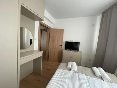 a white bedroom with a bed and a tv at Apartment Park View in Sandanski