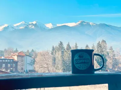 a coffee cup sitting on a window sill with mountains at Mountain view 1-bedroom apartment few steps from ski piste and Gondola lift in Bansko