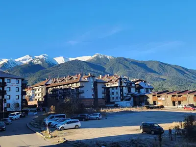 a city with cars parked in a parking lot with mountains at Pirin View Apartment in Bansko