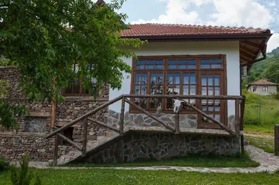 a house with a stone wall and a wooden staircase at Самостоятелна къща за гости с изглед към планината Вила Марк in Kraevo