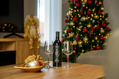 a bottle of wine and two glasses on a table with a christmas tree at Къщи за гости ПАВЛЕВСКИ in Banya