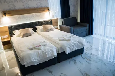 a bedroom with a large bed and a chair at Хотелски комплекс Релакс in Rudozem