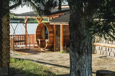a wooden cabin by the water with a tree at Стилни и Луксозни Вили за разпускане in Malo Buchino