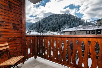 a wooden balcony with a bench and a snow covered mountain at АРТ Къща Широка Лъка in Shiroka Lŭka