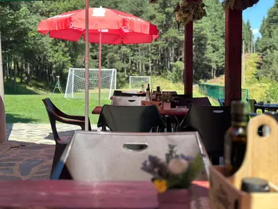 a table with a red umbrella and some tables and chairs at Парк-хотел Родопи in Churen