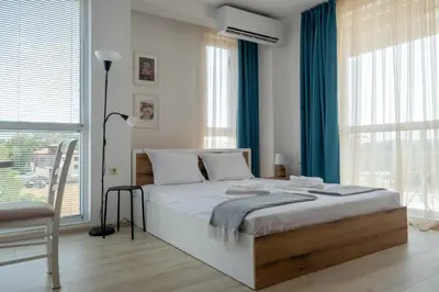 a white bedroom with a large bed with blue curtains at Студио 9 Парк Панорама in Hisarya