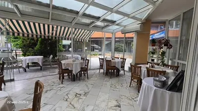 a restaurant with white tables and chairs and windows at Хотел Тото Шанс in Velingrad