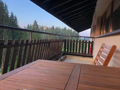 a deck with a wooden table and a chair on a balcony at Panorama Apartment in Pamporovo