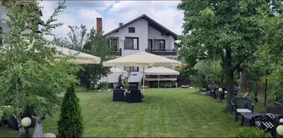 a large white house with chairs and umbrellas in a yard at Guest House Raffe in Dobrinishte