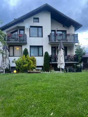 a large white house with an umbrella in the yard at Guest House Raffe in Dobrinishte