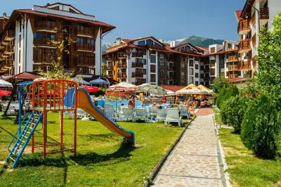 a playground with a slide and chairs and buildings at Апартамент в Белведере Холидей клуб in Bansko