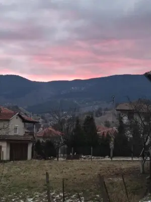 a sunset over a field with houses and mountains at Кулинарна къща за гости СОФРИЦА in Hvoyna