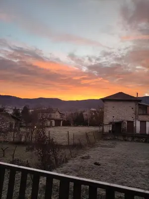 a sunset over a field with a house and a fence at Кулинарна къща за гости СОФРИЦА in Hvoyna