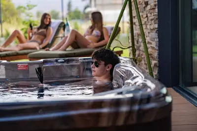 a man in a hot tub with people in the background at Hypnotic Thermal Villas with private SPA in Banya