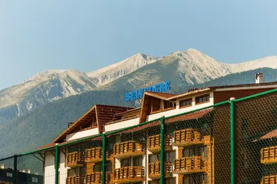 a building with a fence and mountains in the background at Belvedere Bansko - Cozy 1BR - Ski in Winter, Swim in Summer! by Flat Mаnаger in Bansko