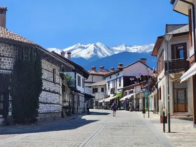 a person walking down a street with mountains in the background at Trinity Apartment & Pool with Spa Near Center in Bansko