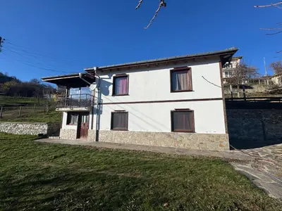 a white house with brown windows on a green field at Guest House in Rhodope Mountains in Rudozem