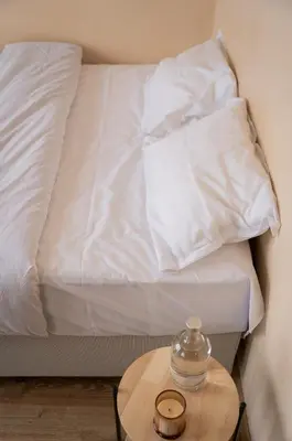 a bed with white sheets and a table with a glass jar on it at Paradise Nest in Sofia