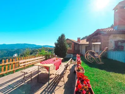 a patio with a table and benches and a house at Вила Зора in Chepelare