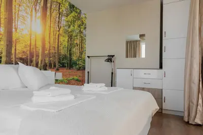 a bedroom with a white bed with a forest view at Просторен апартамент за семейна почивка in Hisarya