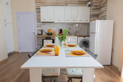 a white kitchen with a white table and chairs at Просторен апартамент за семейна почивка in Hisarya