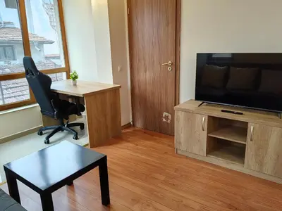 a living room with a television and a chair and a desk at Апартамент Мария in Bansko