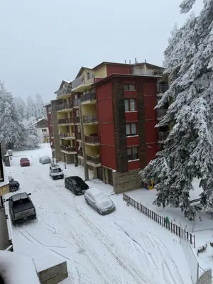 a snow covered parking lot in front of a building at Madzharovi Apartments in Borovets