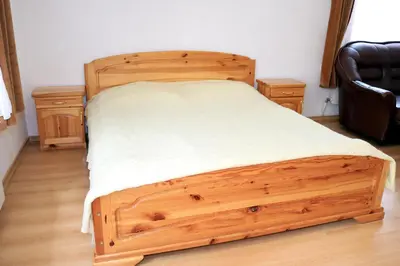 a wooden bed in a room with a black chair at Къща за гости 