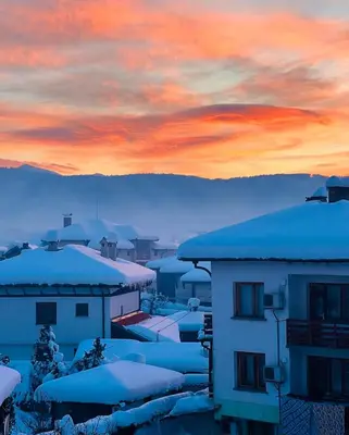 a city with snow covered roofs and a sunset at Cosy Dream Appartment near Borovets in Samokov