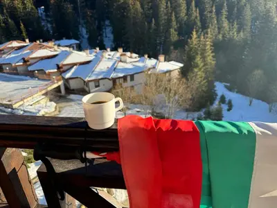 a cup of coffee sitting on a balcony with a snow covered village at Captain's Apartment in Pamporovo