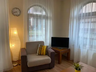 a living room with a chair and a tv and a clock at Cedar Lodge Apartament - Gondola in Bansko