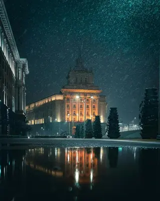 a lit up building with a reflection in the water at night at Angels Loft opposite The Mall in Sofia