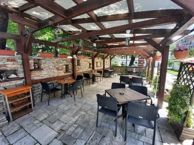 a patio with tables and chairs under a wooden pergola at Семеен хотел-ресторант Маламовата къща in Gotse Delchev