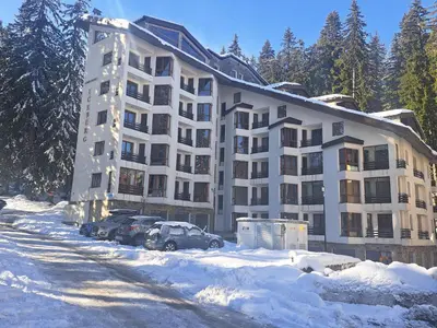 a large apartment building with cars parked in the snow at Alpine Apart Pamporovo in Pamporovo