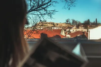 a woman looking out of a window at a city at Kapana - a 106m2 Flat right on the Pedestrian Street in Plovdiv