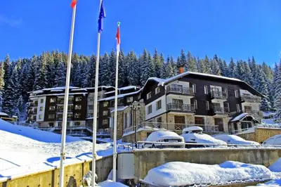 a building in the snow with flags in front of it at Edelweiss Mountain Apartment - Stream Resort Spa & Pool, Pamporovo in Pamporovo