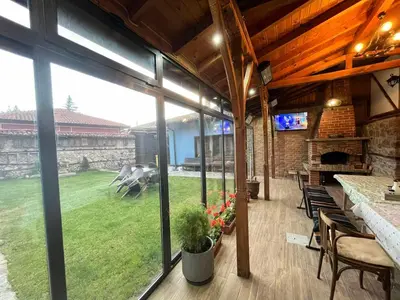 a patio with a table and chairs and a large window at Стаи за гости Царвулджиеви in Koprivshtitsa