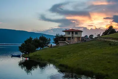 a house on top of a hill next to a lake at Divna Forest & Lake House in Dospat