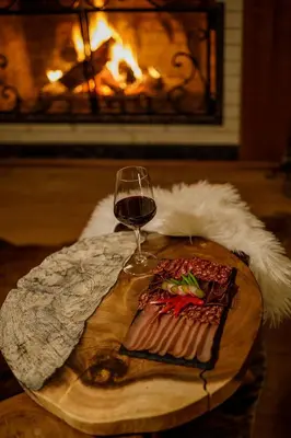 a glass of wine and a plate of food on a table with a fireplace at Green Life Bansko in Bansko