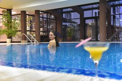a woman in a swimming pool with a drink at Royal Bansko Family Apart Hotel - All Inclusive Light or Half Board & Drinks With Heated Indoor Pool & Jacuzzis in Bansko