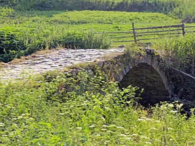 an old stone bridge in the middle of a field at Family hotel Valchanovata Kashta in Fotinovo