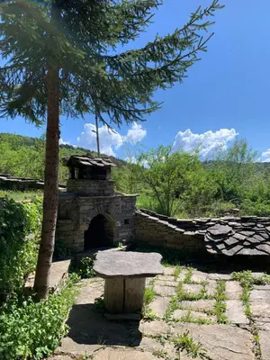 a stone fireplace with a bench next to a tree at Кюповата къща 1860 Qpova house in Kovachevitsa