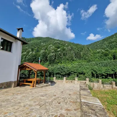 a picnic shelter in front of a building with a mountain at Guest House Ivan in Cherni Osŭm