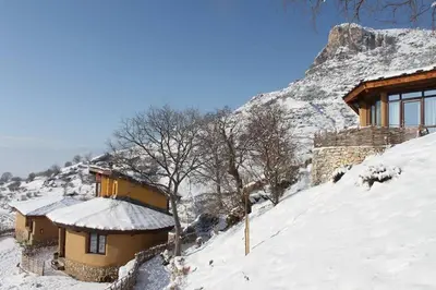 a house on a snow covered hill with a mountain at Eco Village Under the Cliffs in Ilindentsi