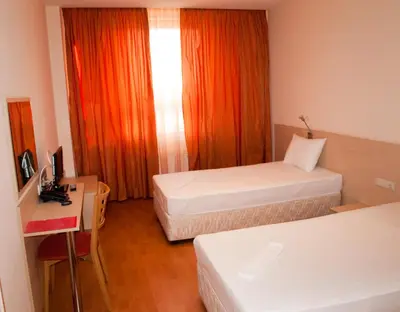 a room with two beds and a desk and a window at Hotel Astra in Sofia