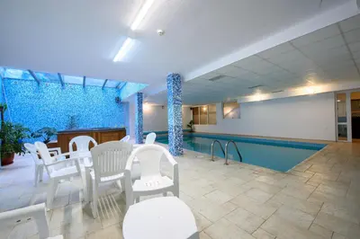 a swimming pool with white chairs and a table at Kap House Family Hotel in Bansko