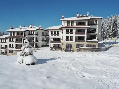 a building in the snow with a snow covered yard at High Five Villas in Pamporovo