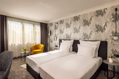 a bedroom with a large bed and a yellow chair at Rosslyn Thracia Hotel Sofia in Sofia