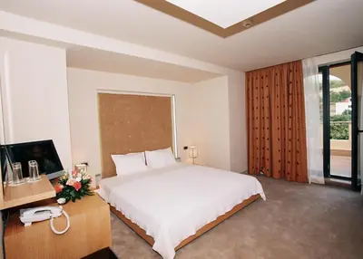 a bedroom with a white bed and a desk with a phone at Park Hotel Sandanski in Sandanski