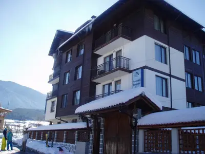 a building with snow on the ground in front of it at Apartments & Studios Mountain Romance in Bansko